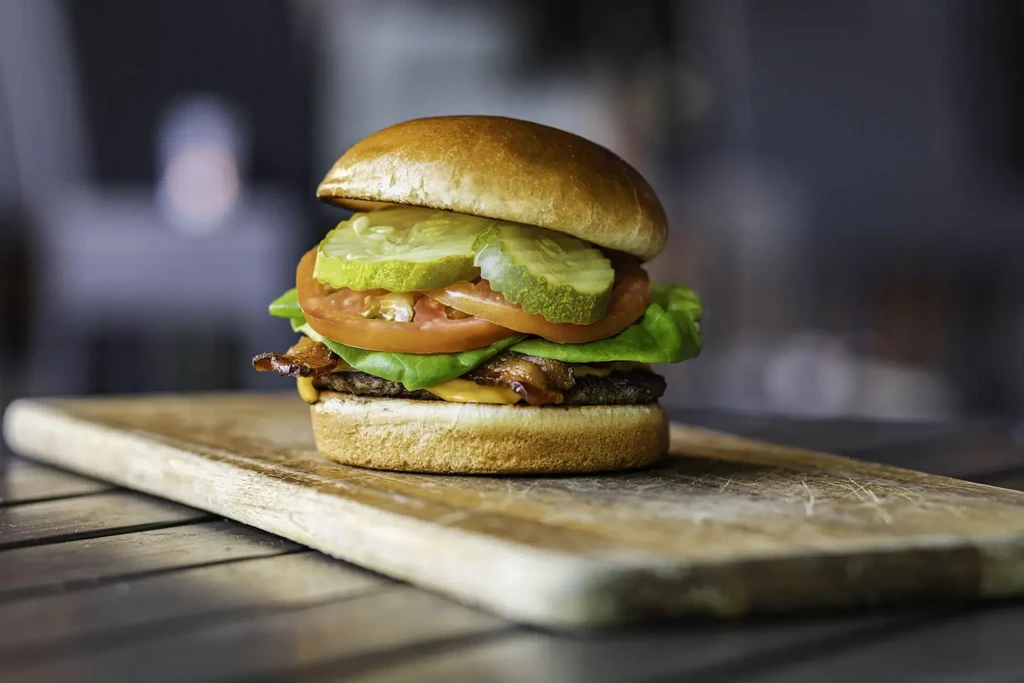 Stacked gourmet bacon cheeseburger on a rustic wooden cutting board.