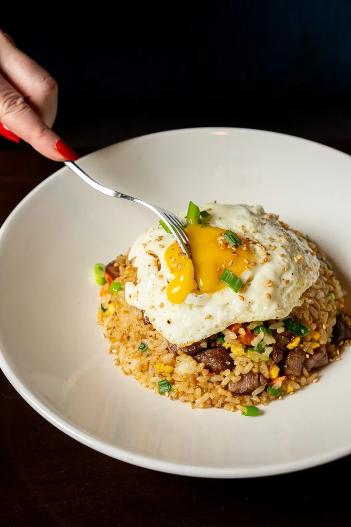 Fried rice topped with a runny fried egg, pierced by a fork.