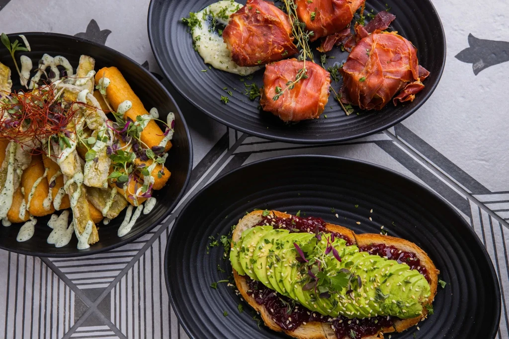 Three artfully presented dishes: fried sticks, prosciutto-wrapped meat, and avocado toast.