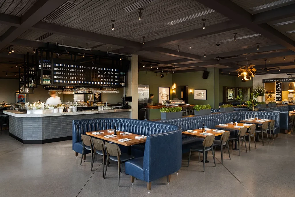 Modern restaurant interior with navy booths, a raw bar, and gold chandelier.