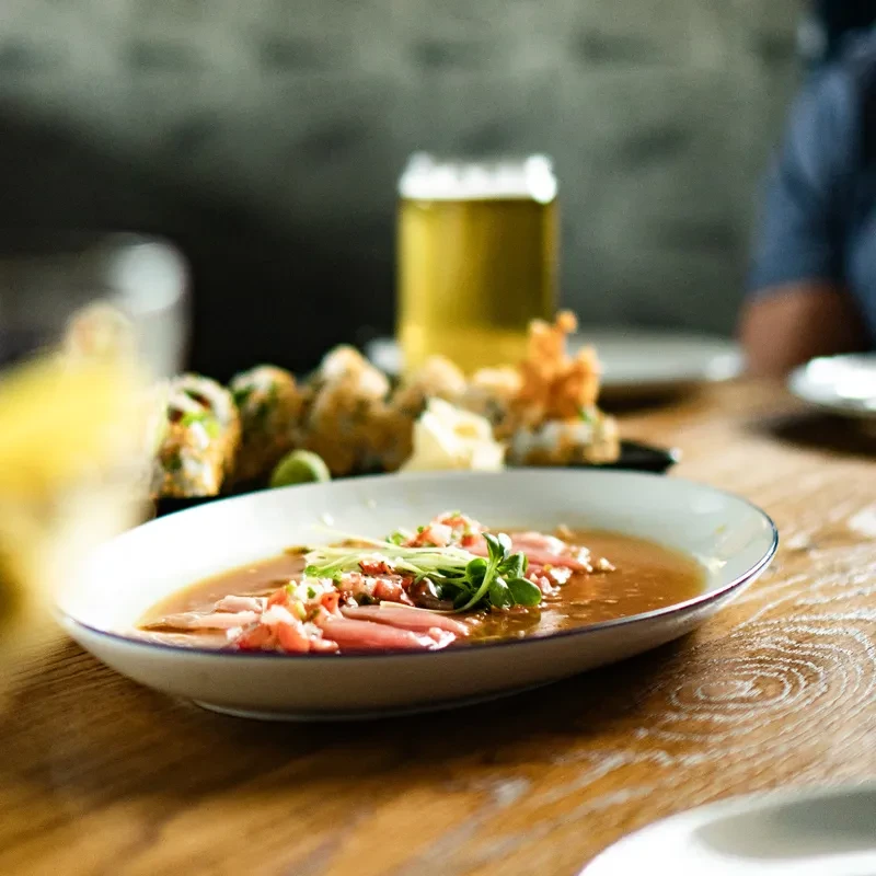 Red meat dish with microgreens, blurred sushi and beer on a table.