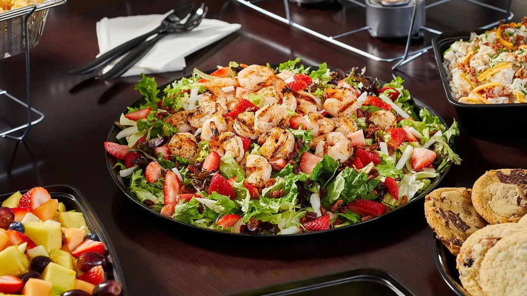 A buffet table with grilled shrimp, strawberry salad, fruit, and cookies.