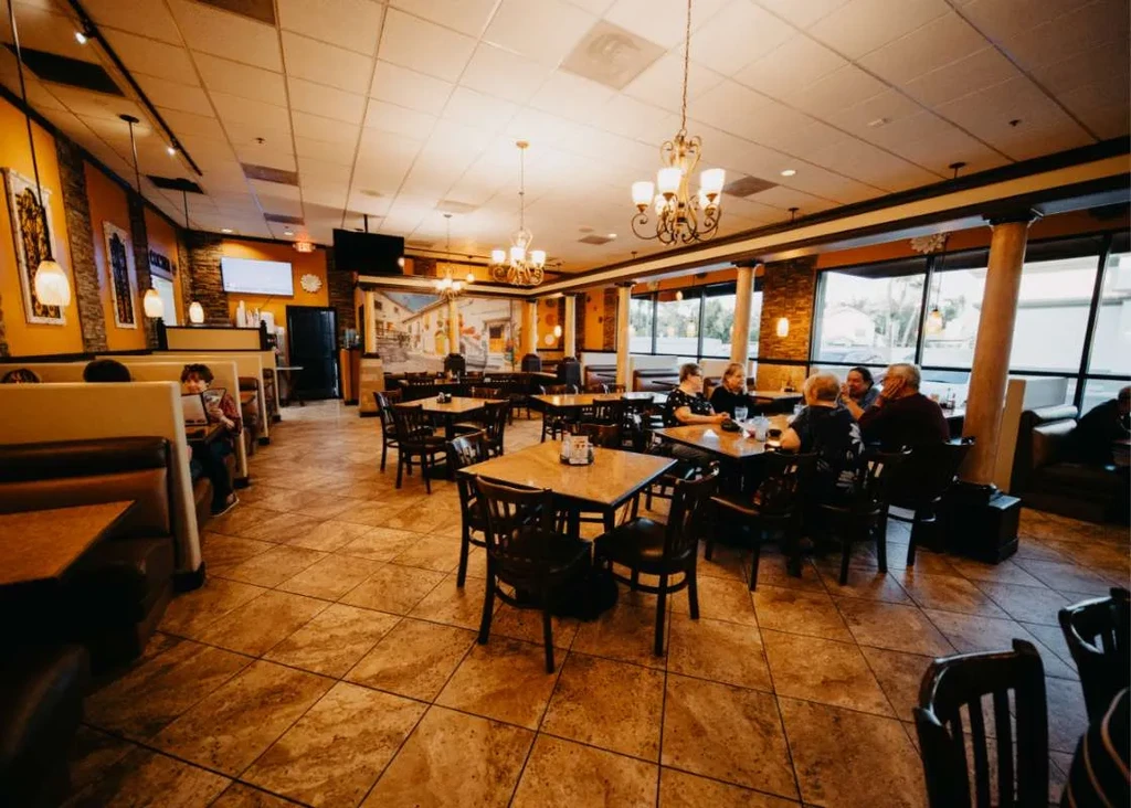 Restaurant interior: booths, tables, mustard walls, ornate chandeliers, some diners.