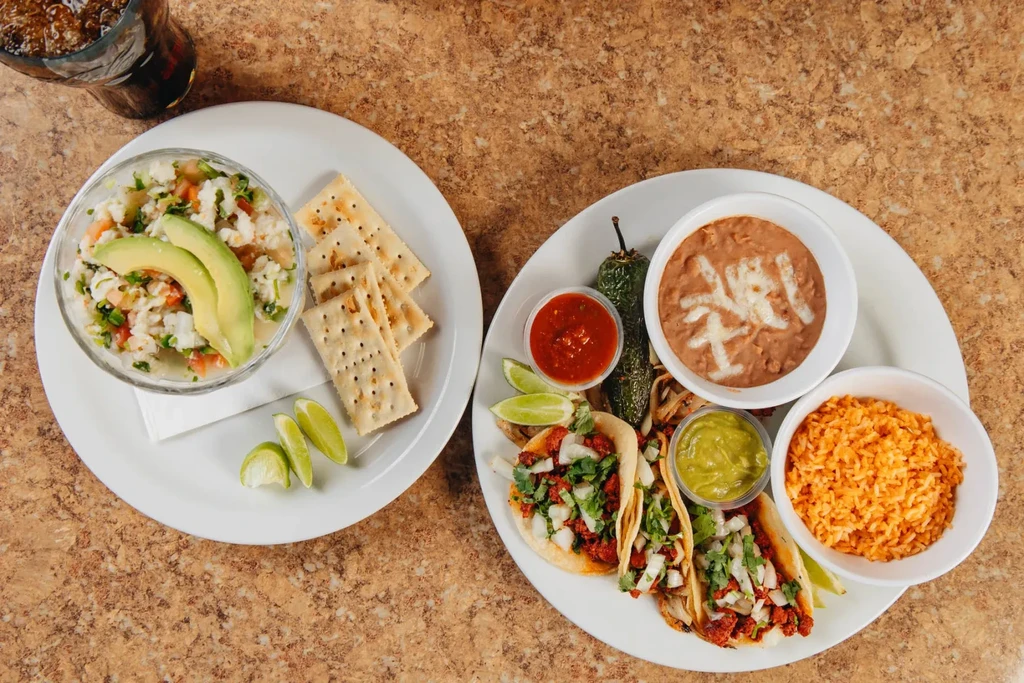 Two plates of Mexican food: ceviche, tacos, rice, beans, and drink.