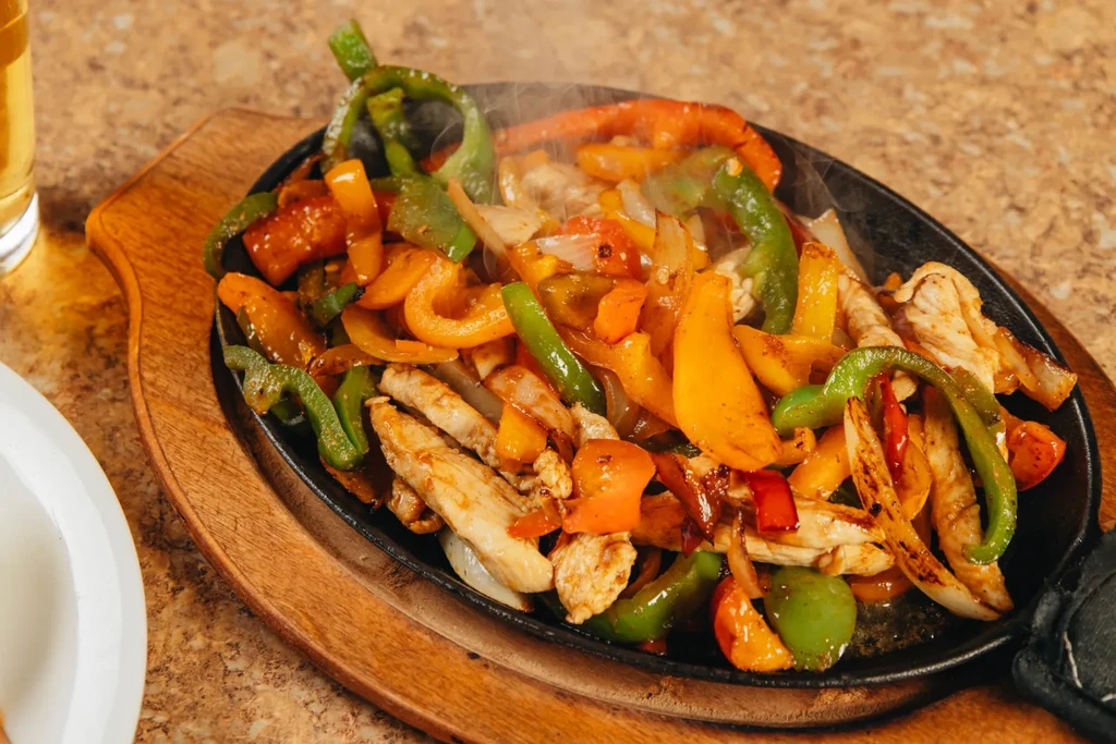 Sizzling chicken fajitas with peppers and onions on a cast iron skillet.