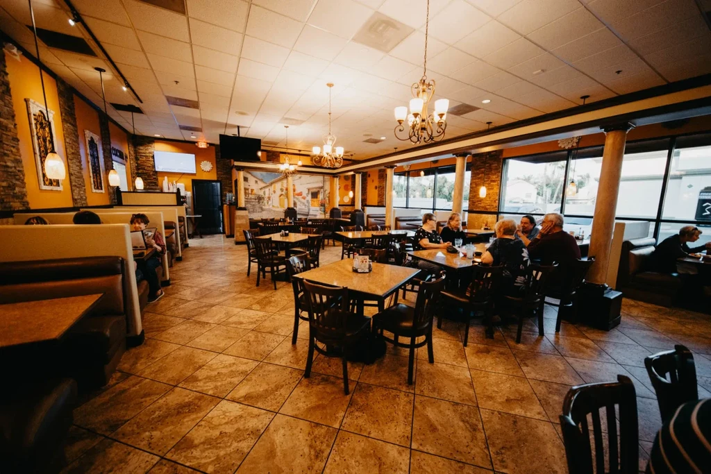 Vibrant, warmly lit restaurant dining room with tables, booths, and diners.