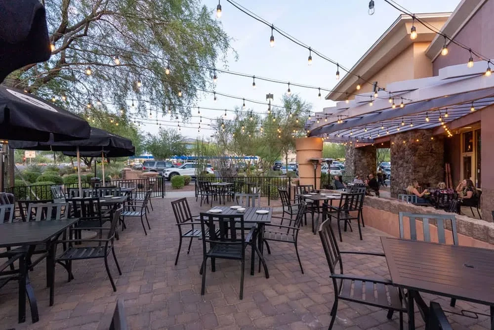 Outdoor restaurant patio with empty tables, umbrellas, and string lights.