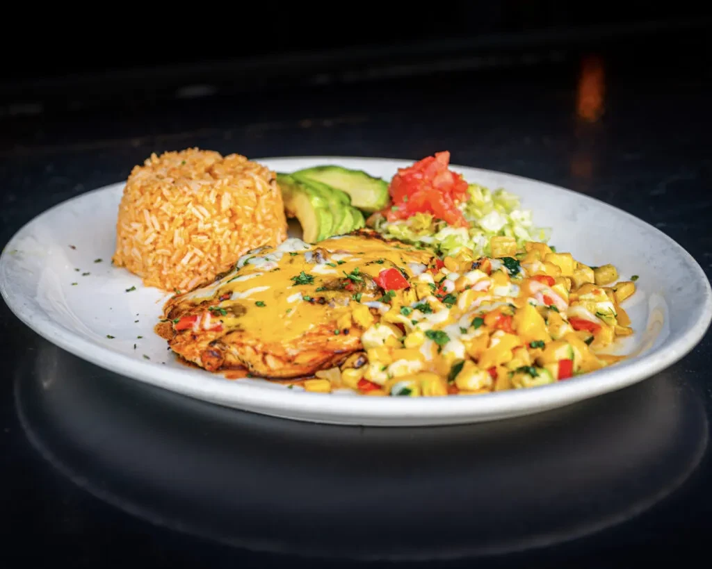 Grilled chicken with cheese, orange rice, corn salad, avocado, and tomatoes.