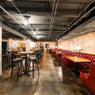 Empty industrial-chic restaurant with high-top tables and red leather booths.