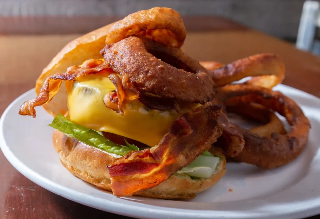 Close-up of a burger topped with cheese, bacon, lettuce, and onion rings.