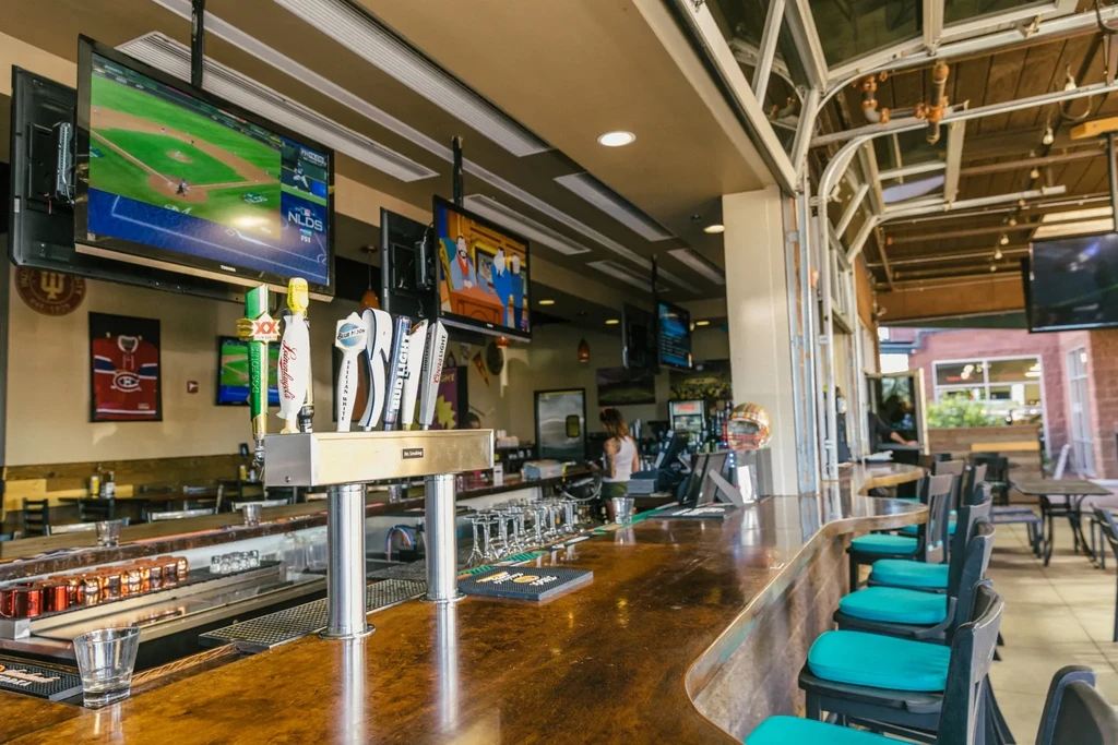 Sports bar interior: wooden bar, beer taps, multiple TVs, visible patio.