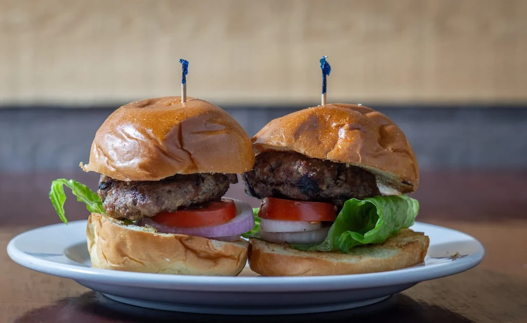 Two grilled mini burgers with fresh toppings and blue food picks.