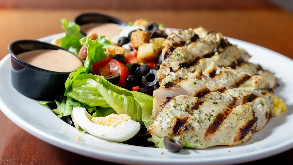 Grilled chicken salad with lettuce, tomatoes, olives, egg, and dressing.