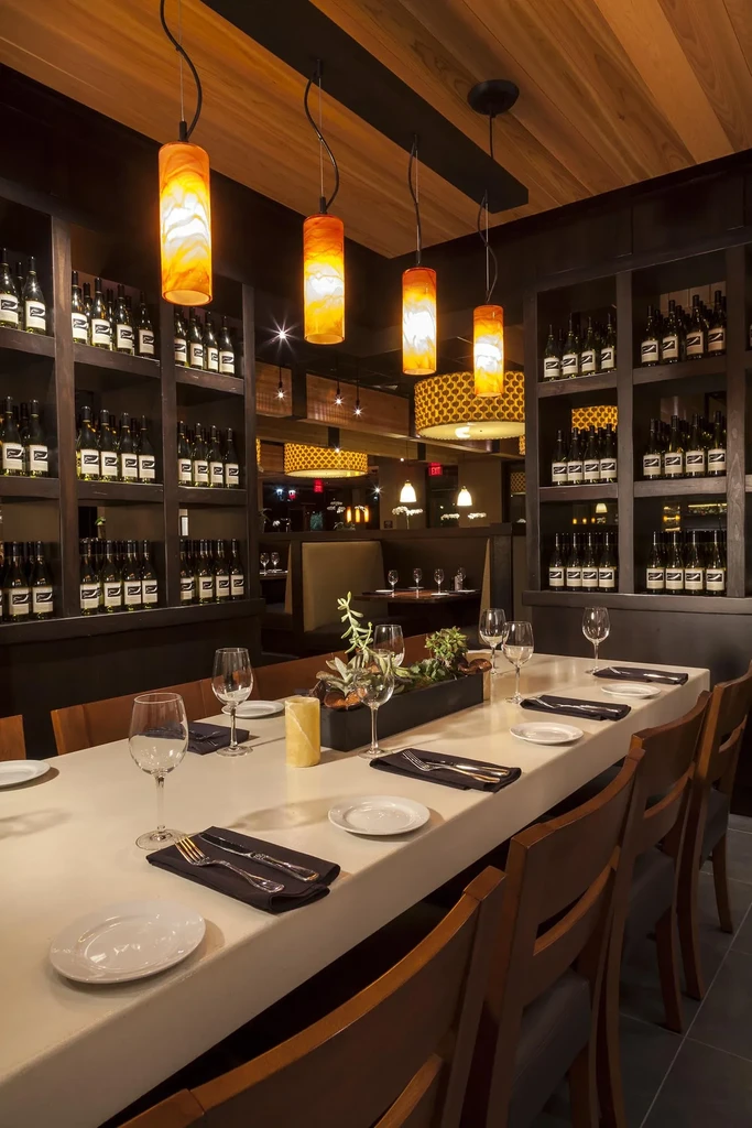 Warmly lit restaurant interior with long communal table and wine shelves.