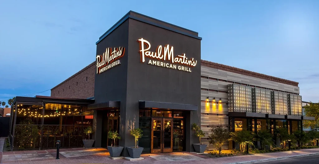 Paul Martin's American Grill, modern exterior with illuminated signs at dusk.