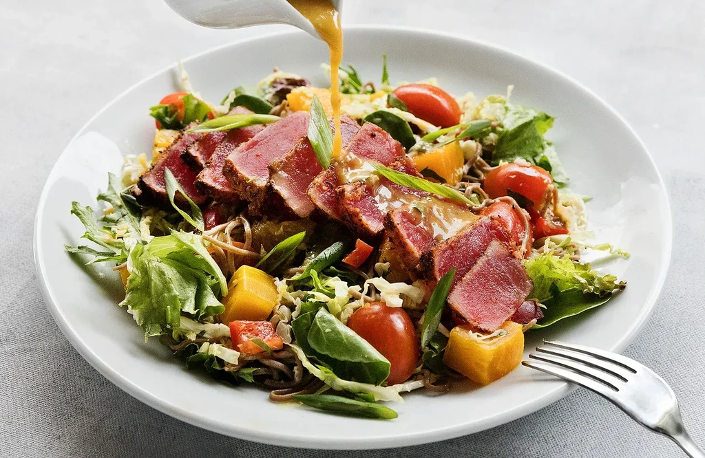 Seared tuna salad with greens, tomatoes, mango, noodles, dressing poured.