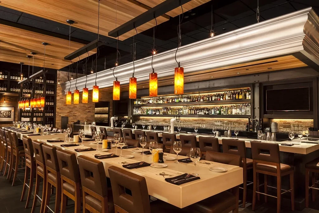 Empty upscale restaurant bar with communal table and warm amber lighting.