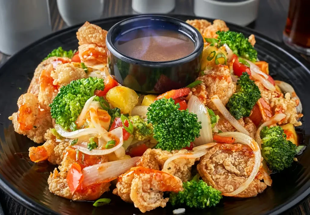 Vibrant fried chicken and vegetables with sauce on a dark plate.