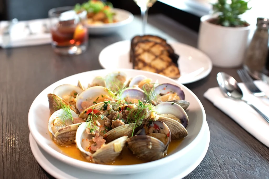 Steamed clams in orange broth with herbs and crumbled sausage.