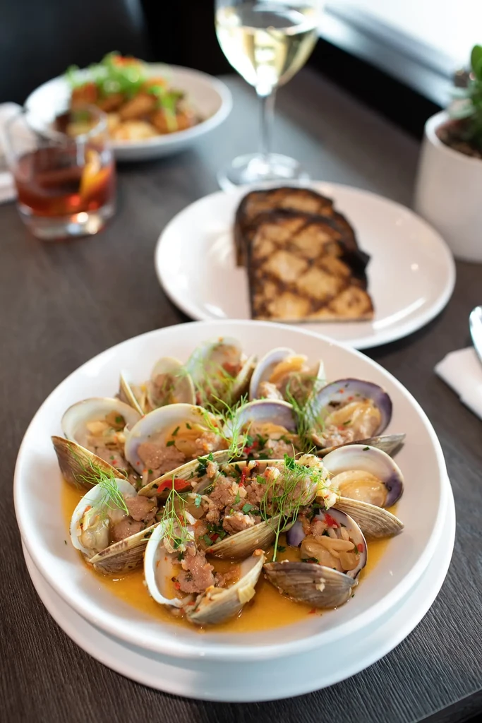 Steamed clams in yellow broth, garnished with herbs, grilled bread and drinks.