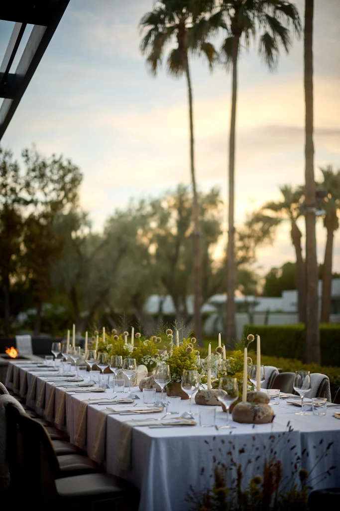 Long outdoor dining table with flowers, candles, and warm golden light.