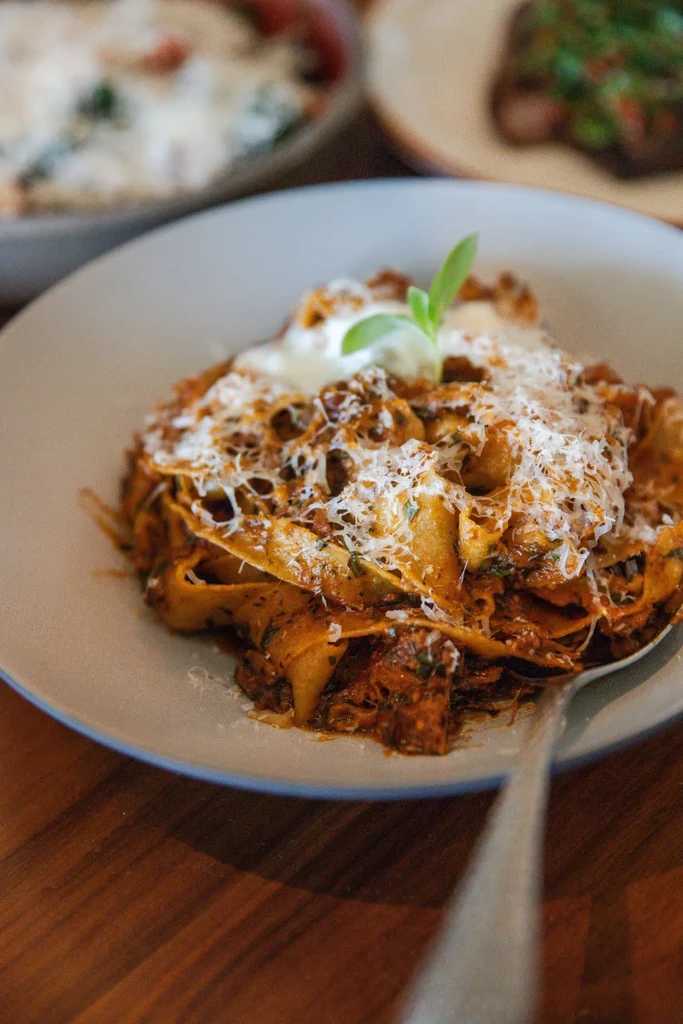 Pappardelle pasta with meat ragu, grated cheese, cream, and basil.