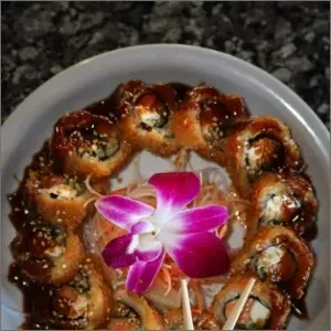 Deep-fried sushi rolls with dark sauce, sesame seeds, and orchid garnish.