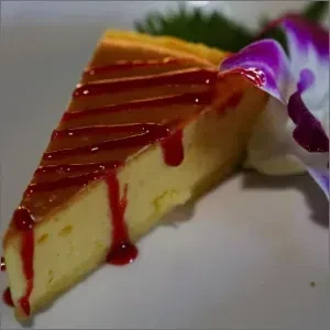A close-up slice of cheesecake with caramel, red berry sauce, and orchid.