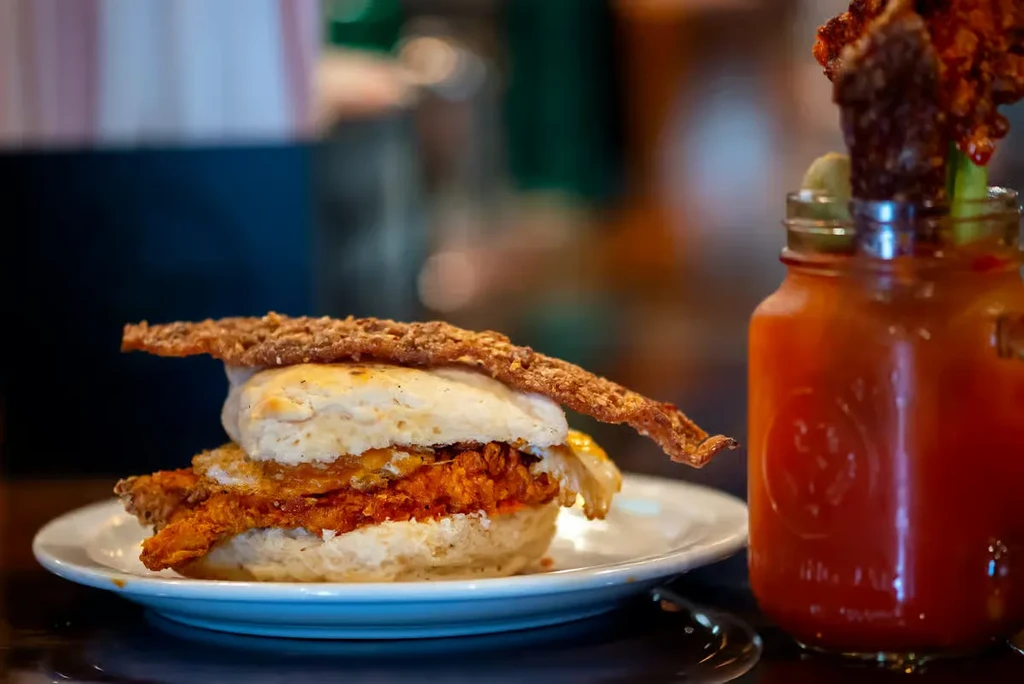 Well-lit chicken biscuit sandwich, fried egg, and Bloody Mary.
