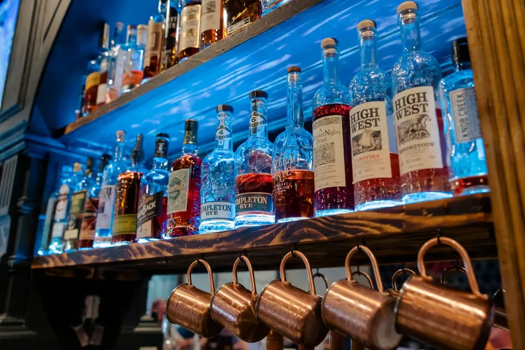 Well-lit bar shelves display liquor bottles with blue backlighting and copper mugs.