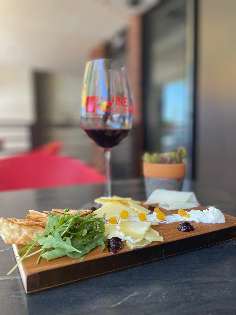 Rustic wooden board with cheeses, crackers, arugula, and red wine glass.
