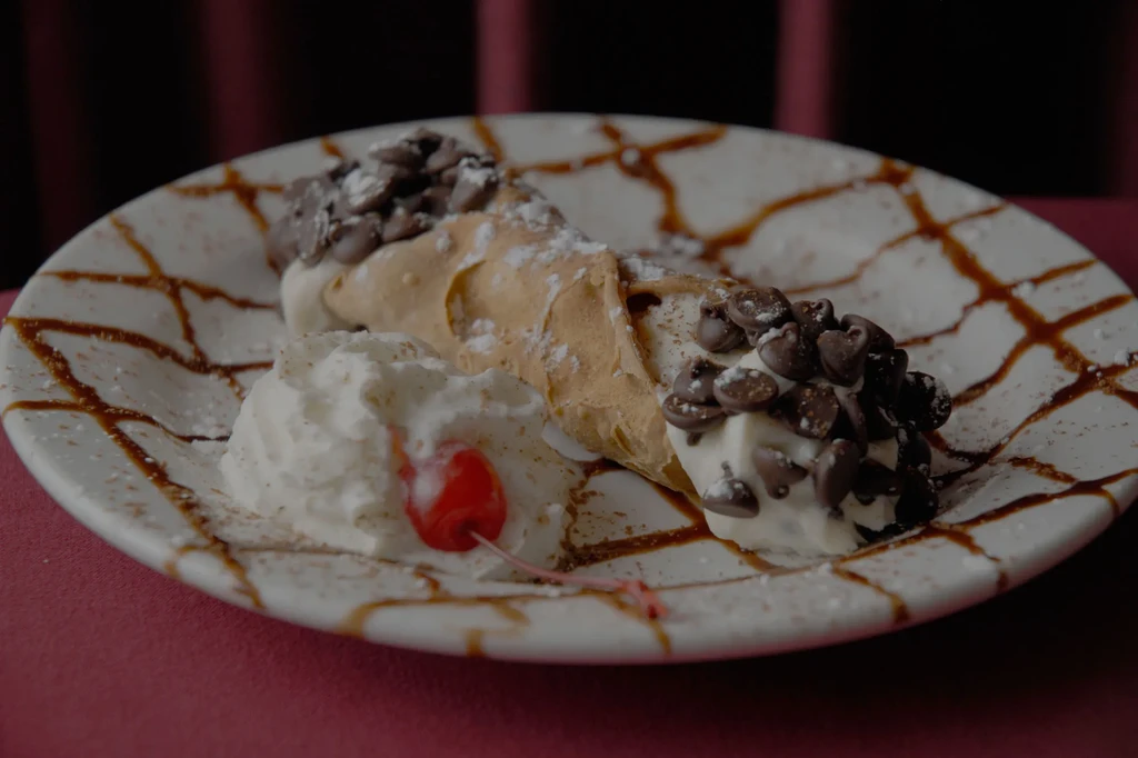 Cream-filled cannoli with chocolate chips, powdered sugar, whipped cream, and cherry.