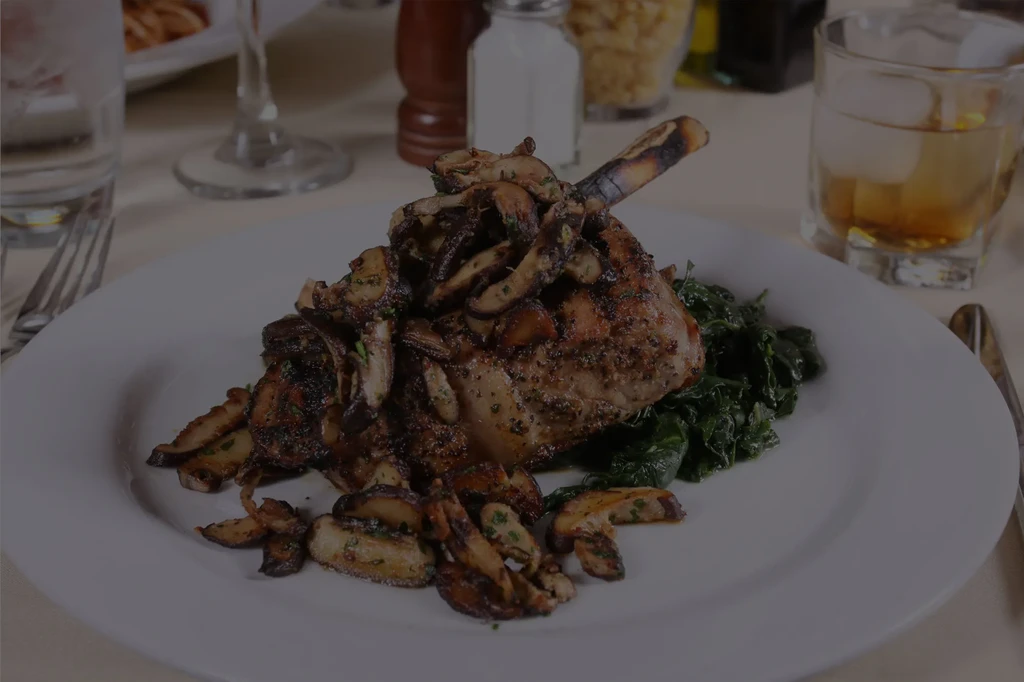 Plated bone-in meat chop with mushrooms and greens at a restaurant.