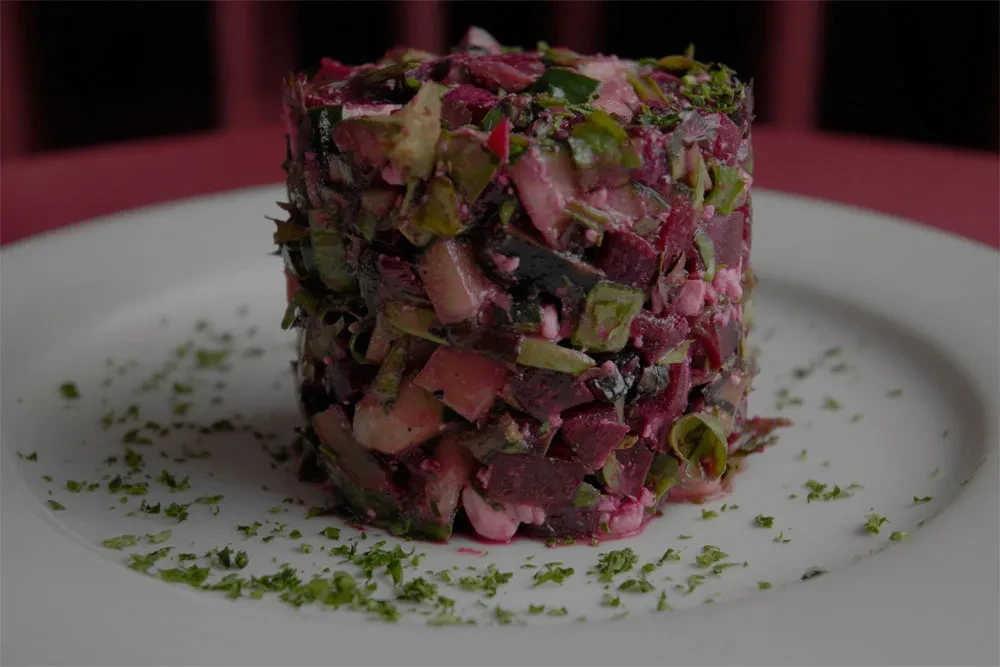 Cylindrical stack of diced beetroot, cheese, and herbs on a plate.