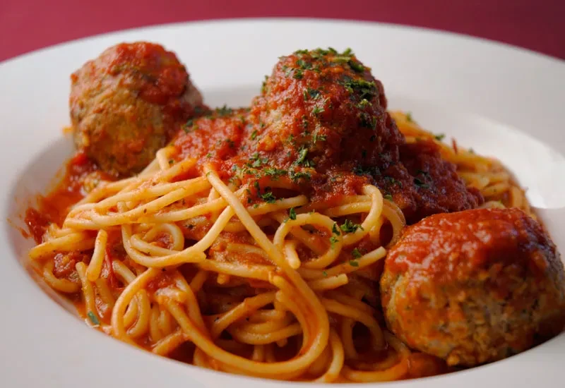 Close-up of spaghetti and three meatballs with sauce and herbs.