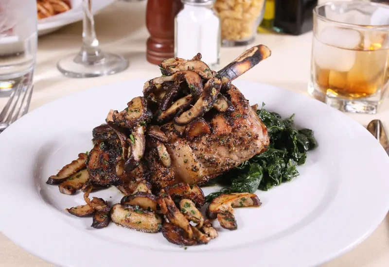 Plated meat chop with mushrooms and greens in a restaurant.
