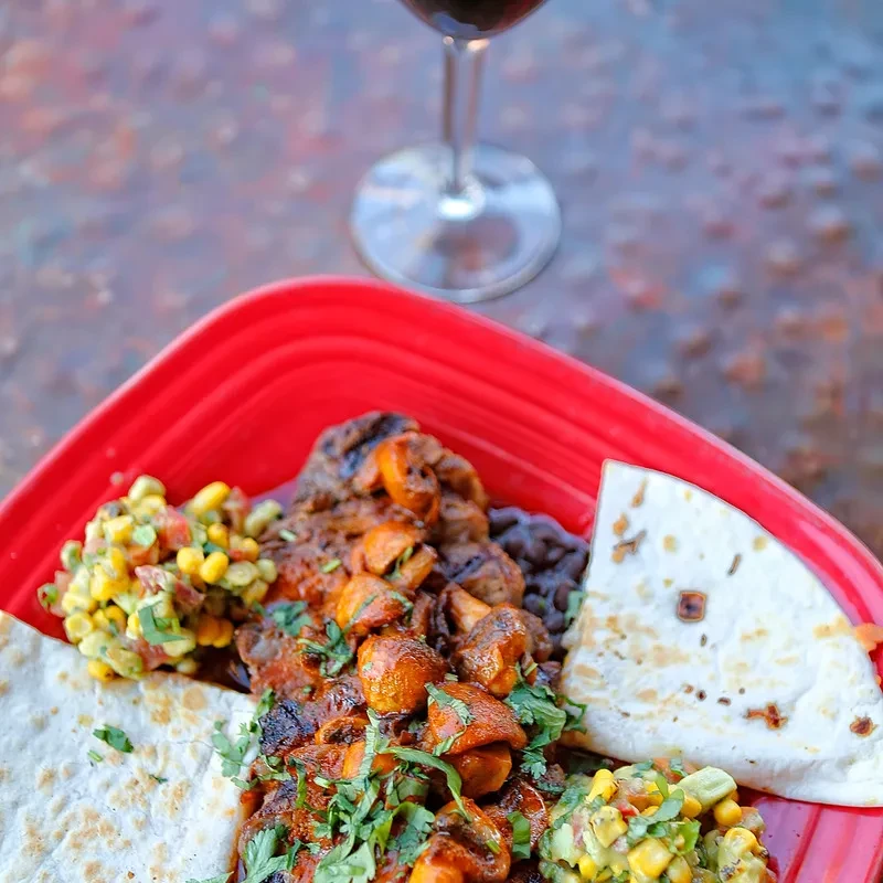 Vibrant Mexican meal with mushrooms, beans, corn salsa on red plate.