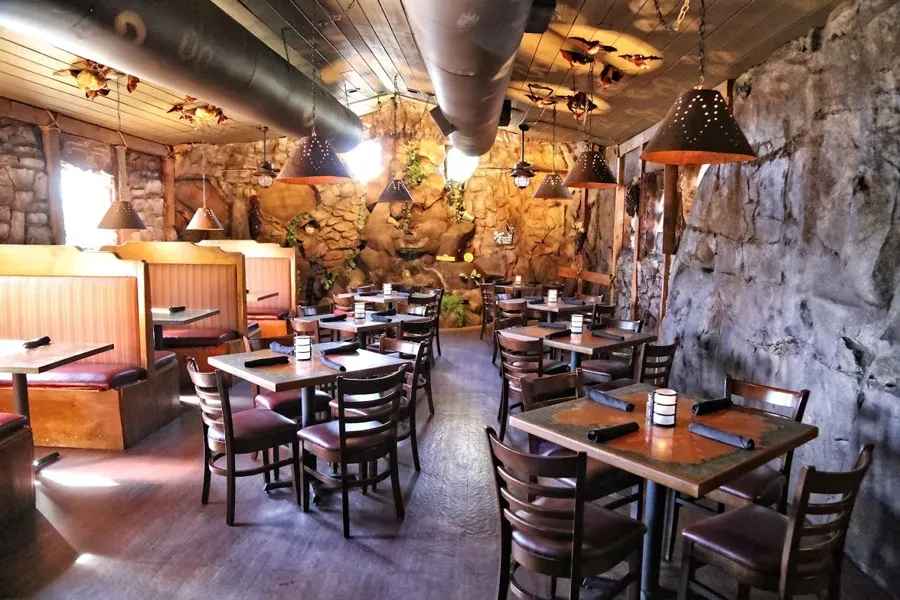 Empty rustic restaurant interior with rock walls and warm lighting.