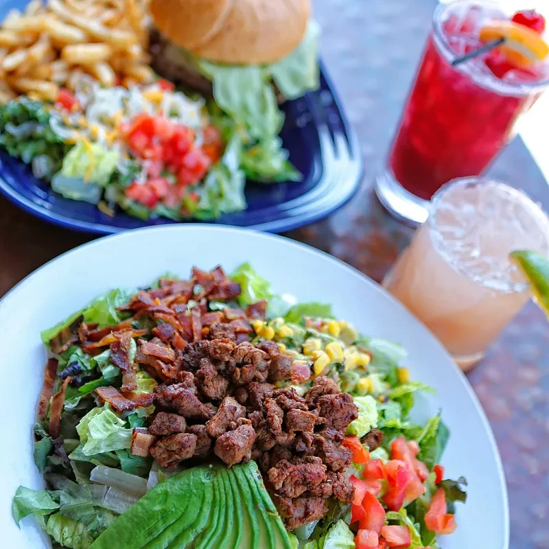 High-angle view of a hearty salad, burger, fries, and two drinks.