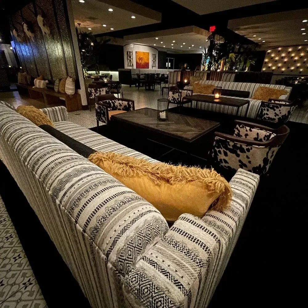 Dimly lit lounge with striped sofa, cowhide chairs, candles, and plants.