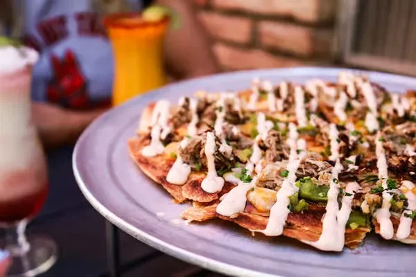 Loaded flatbread or nachos with meat, green chunks, and creamy sauce.