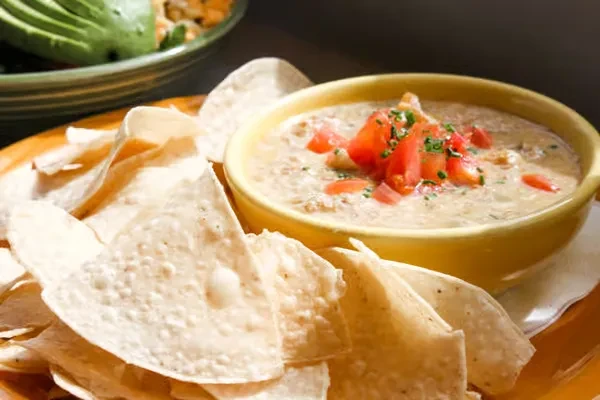 Creamy queso dip with tomatoes and herbs, surrounded by tortilla chips.