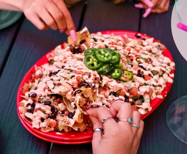 Hands scooping diced protein, beans, jalapeños from a red platter.