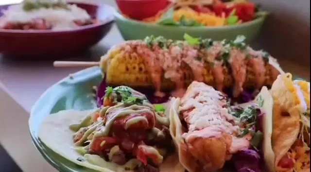 Vibrant plate of three tacos, elote, and other Mexican dishes.