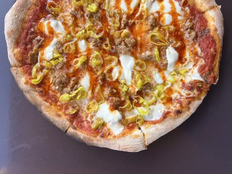Close-up of baked pizza with mozzarella, sausage, peppers, and orange drizzle.