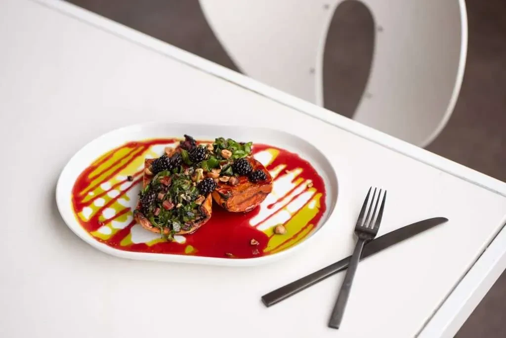 Roasted sweet potato halves with greens, blackberries, sauces, and cutlery.