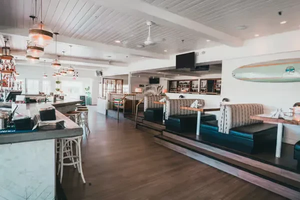 Empty restaurant interior with a long bar, booth seating, and coastal decor.