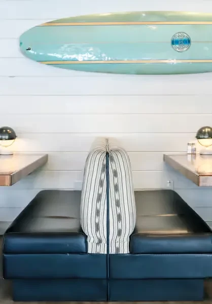 Bright restaurant interior with a blue booth, tables, and surfboard decor.