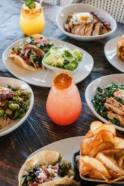 Colorful cocktails, tacos, salads, and fries on a wooden table.