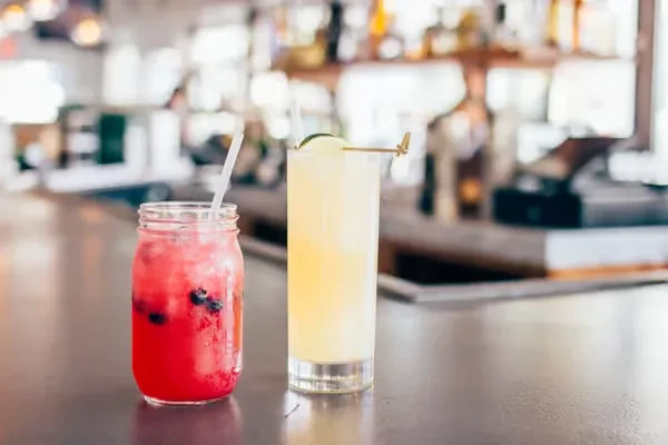 Two brightly colored drinks on a dark bar top, blurred background.